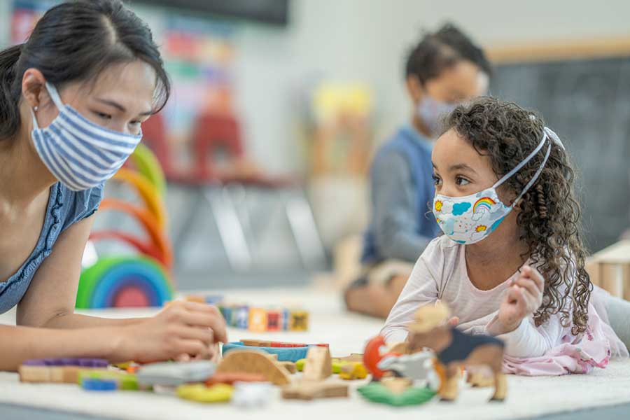 Teacher and child wearing masks while playing with blocks