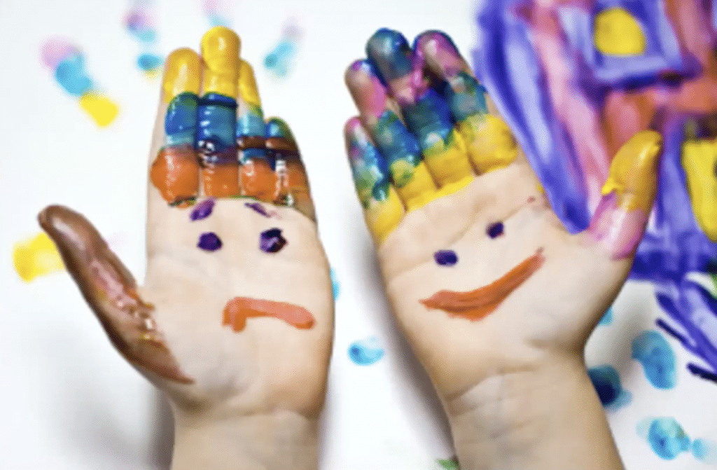 Two young hands with a smiley face and frowny face painted on them