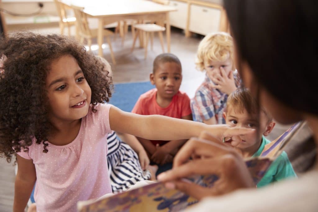 Pupils At Montessori School Looking At Book With Teacher